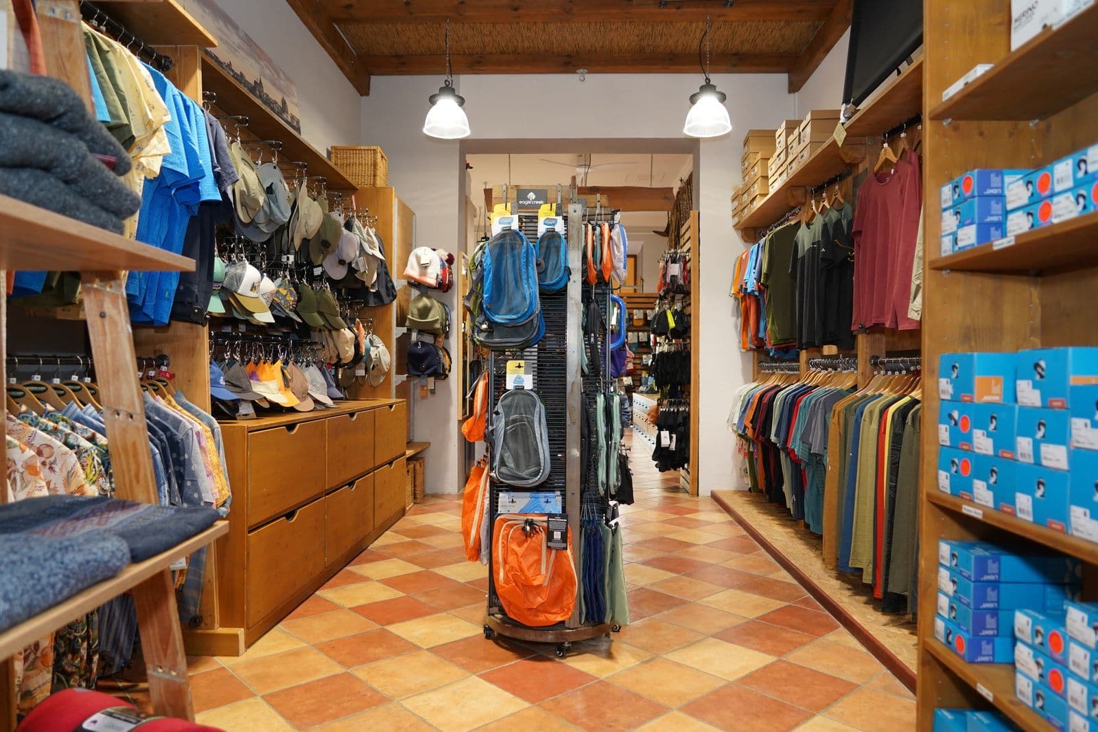 Innenaufnahme eines Outdoor- und Sportfachgeschäfts mit Holzregalen, Kleidung, Rucksäcken und Ausrüstung.